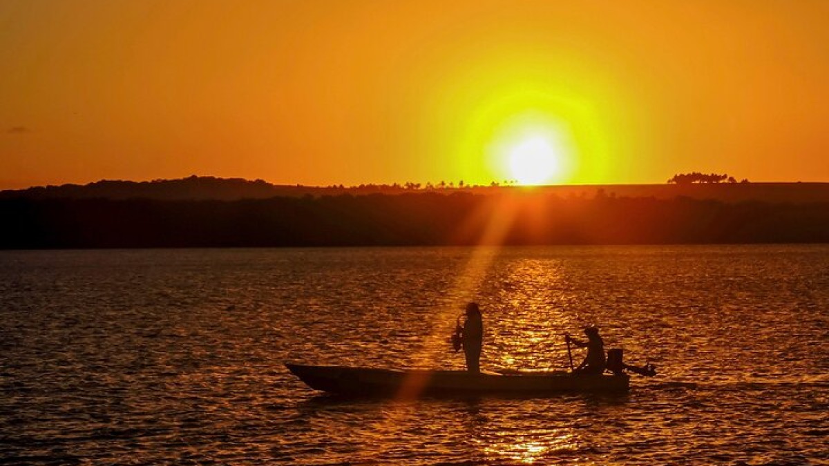 Pescadores em uma canoa recortados contra o sol alaranjado do fim de tarde no Pantanal