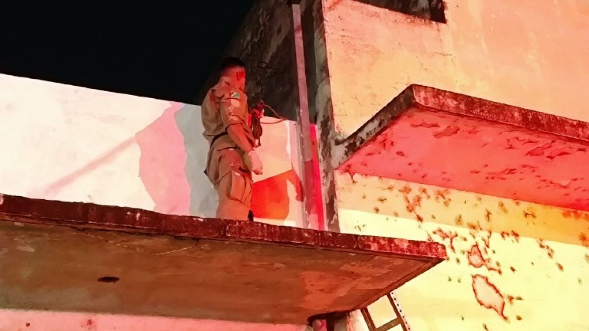 Bombeiro sobre a marquise de um prédio em Corumbá, com escada apoiada na parede, durante resgate noturno