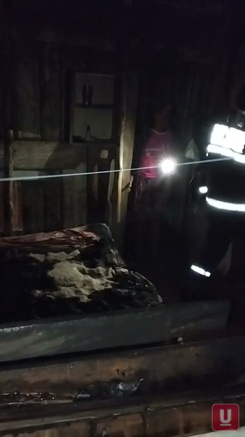 Bombeiros inspecionam com lanternas as vigas e tábuas escurecidas pelo fogo no interior da casa de madeira, no bairro Guaicurus.